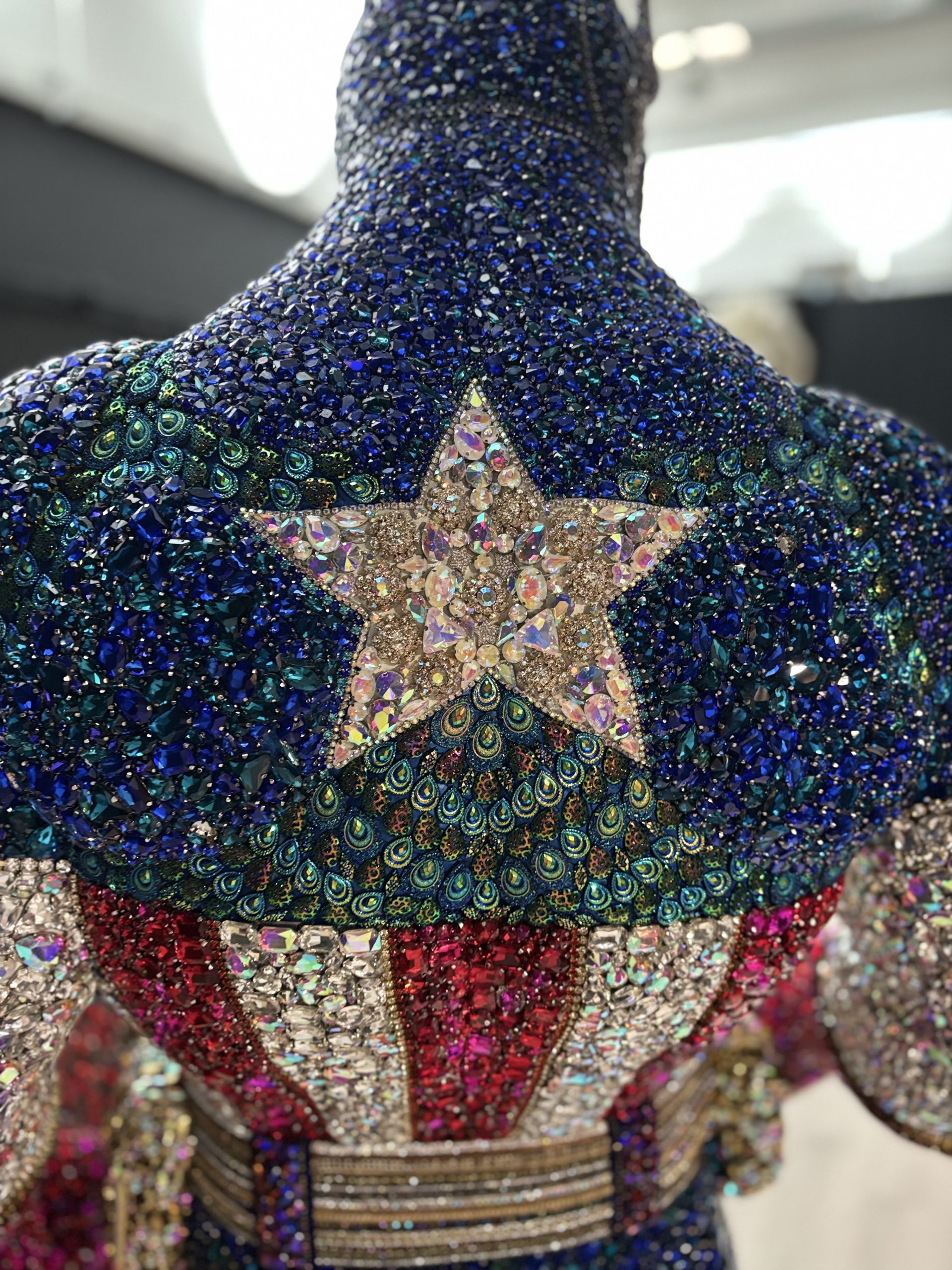 Dettaglio ravvicinato di una scultura decorativa rivestita con strass blu, cristalli luminosi e una stella centrale, con motivi ispirati alle piume di pavone.